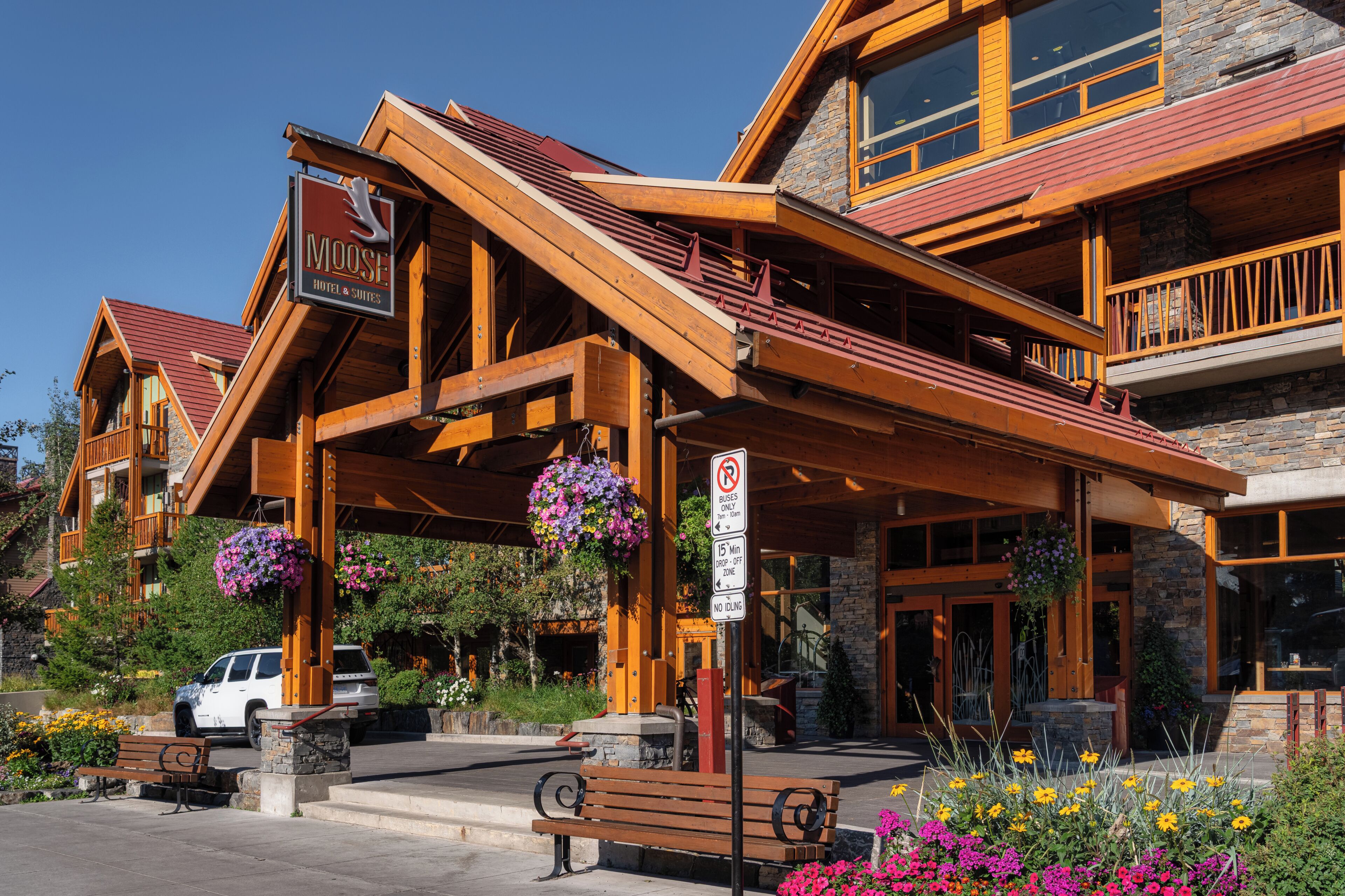 A hotel with a wooden facade, a signboard, and a parking area with a bench.