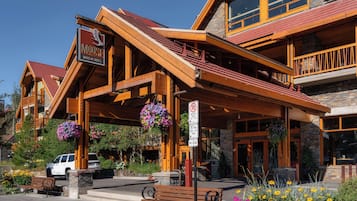 A hotel with a wooden facade, a signboard, and a parking area with a bench.