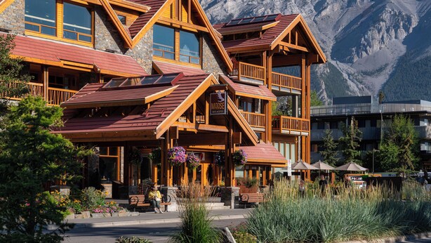 A wooden lodge with multiple balconies, a stone facade, and a mountain backdrop.