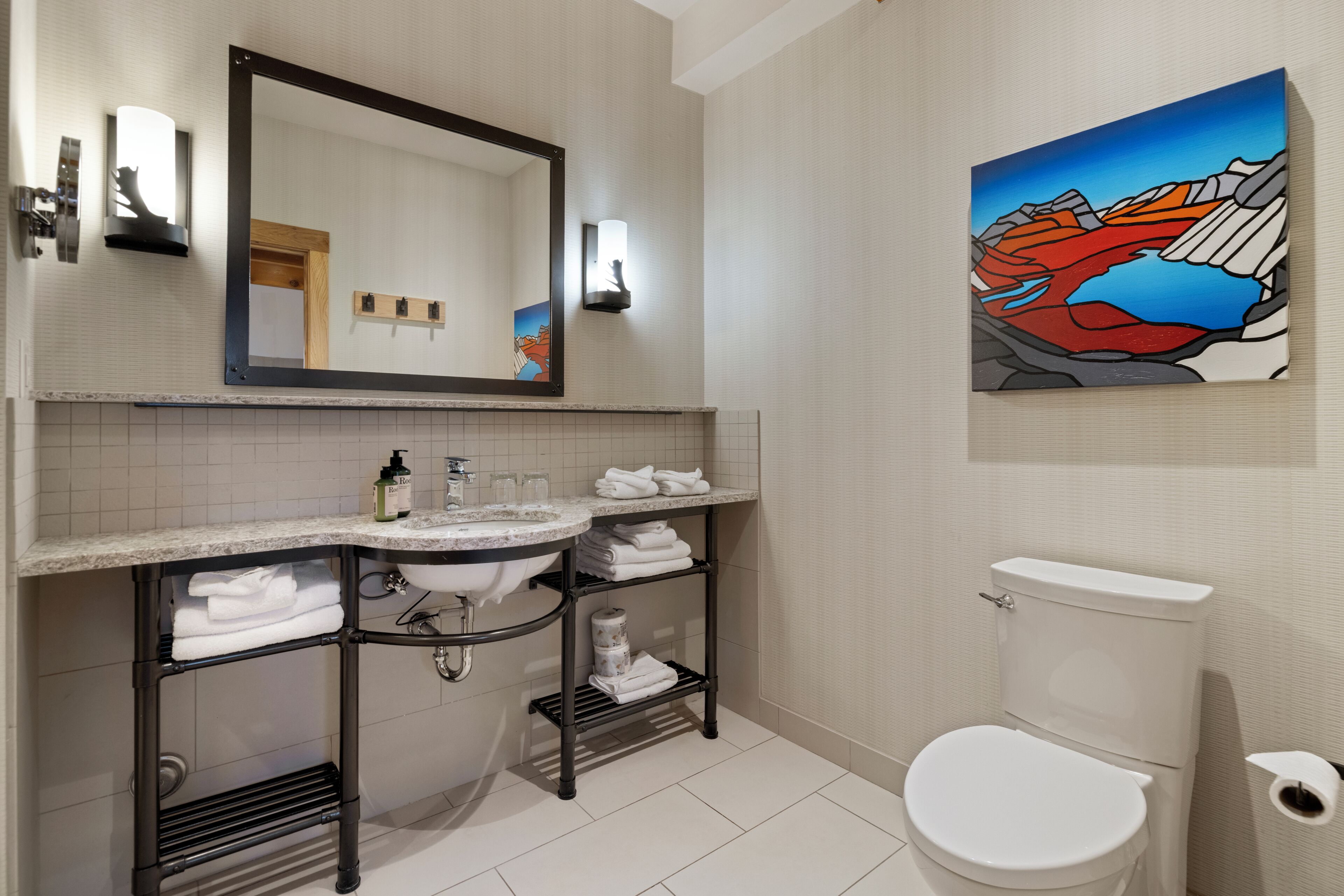A bathroom with a sink, mirror, towel rack, toilet, and a painting on the wall.