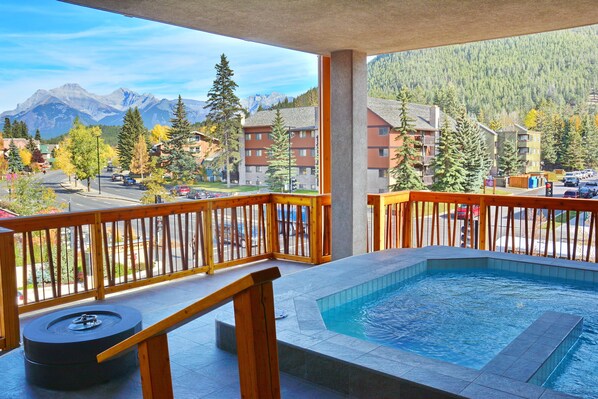 Un balcon doté d’un jacuzzi, d’une balustrade en bois et offrant une vue sur une chaîne de montagnes et des bâtiments.