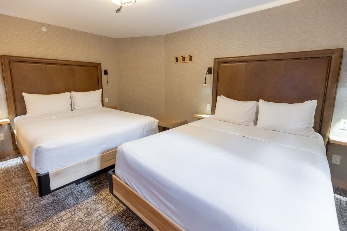 Une chambre d’hôtel avec deux lits simples, des têtes de lit en bois, du linge de lit blanc et une moquette à motifs.