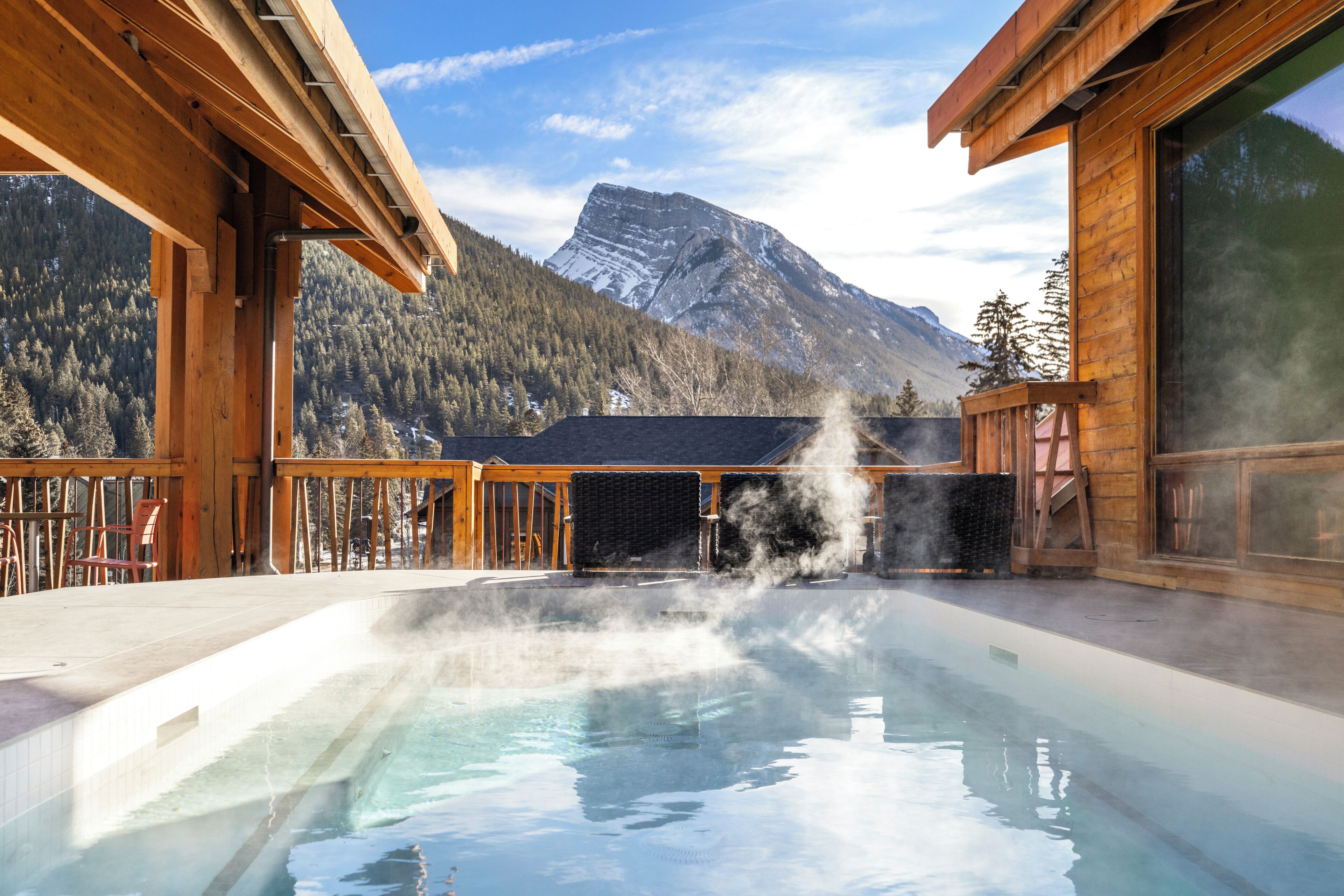 Ein Whirlpool mit aufsteigendem Dampf, umgeben von einer Holzdielenterrasse und Blick auf die Berge.