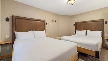 A hotel room with two beds, a wooden headboard, a nightstand, a wall-mounted lamp, and a carpeted floor.