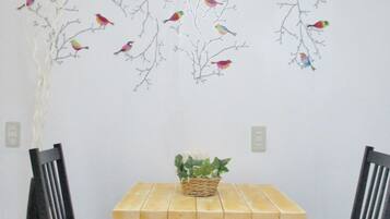 A dining area with a wooden table and two black chairs. There is a wall decoration of colorful birds on branches.