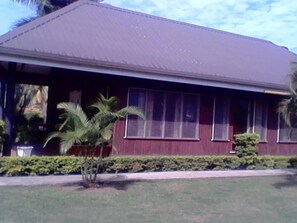 A single-story house with a dark roof, large windows, and a small front yard with a palm tree and shrubs.