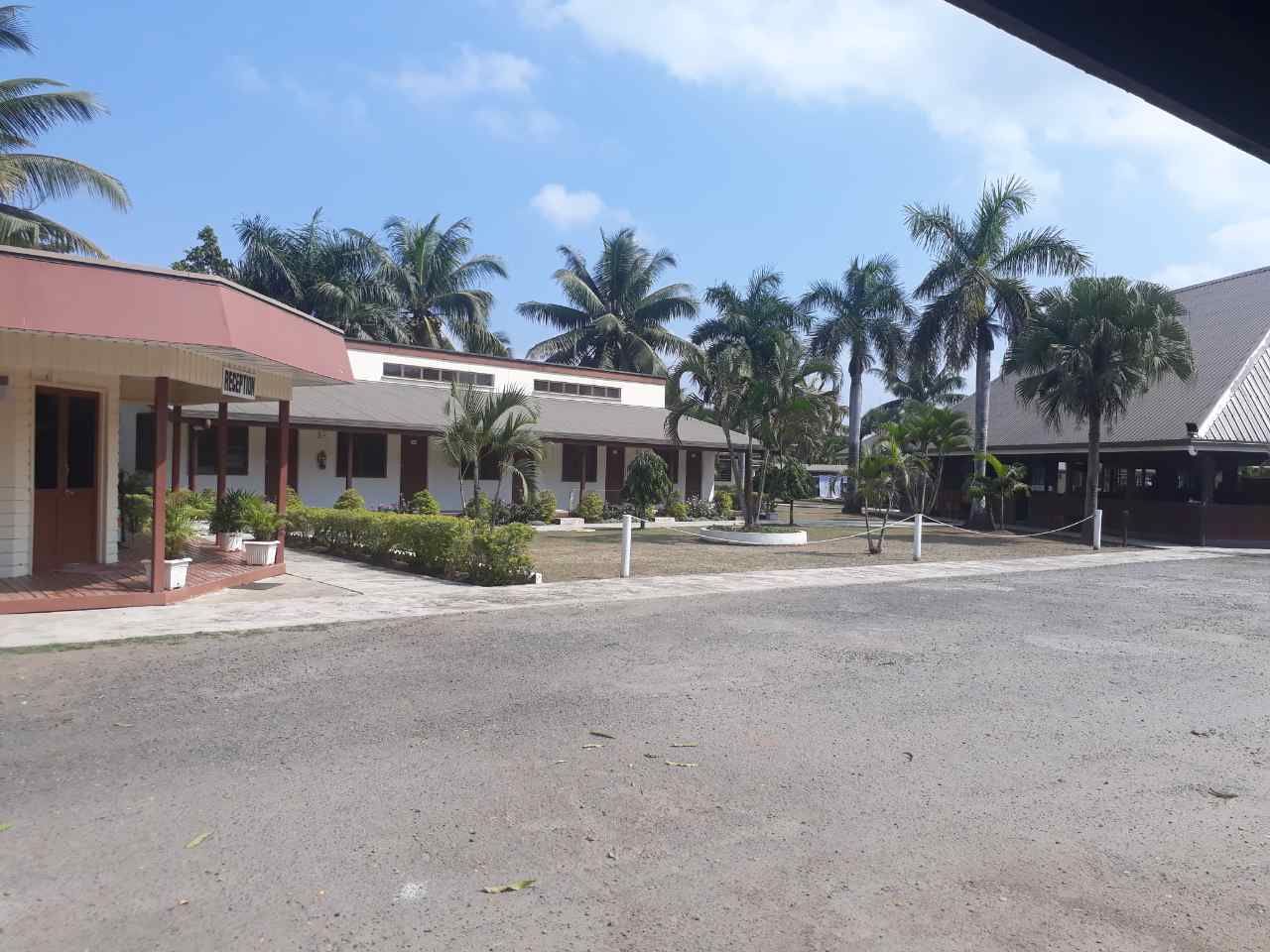 A building with a red roof and a sign that reads "RESERVATION". There are palm trees and a paved area in front of the building.