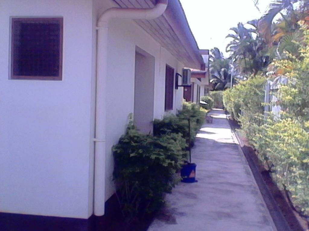 A narrow, straight pathway flanked by white buildings with dark windows and doors, leading to a gated entrance.