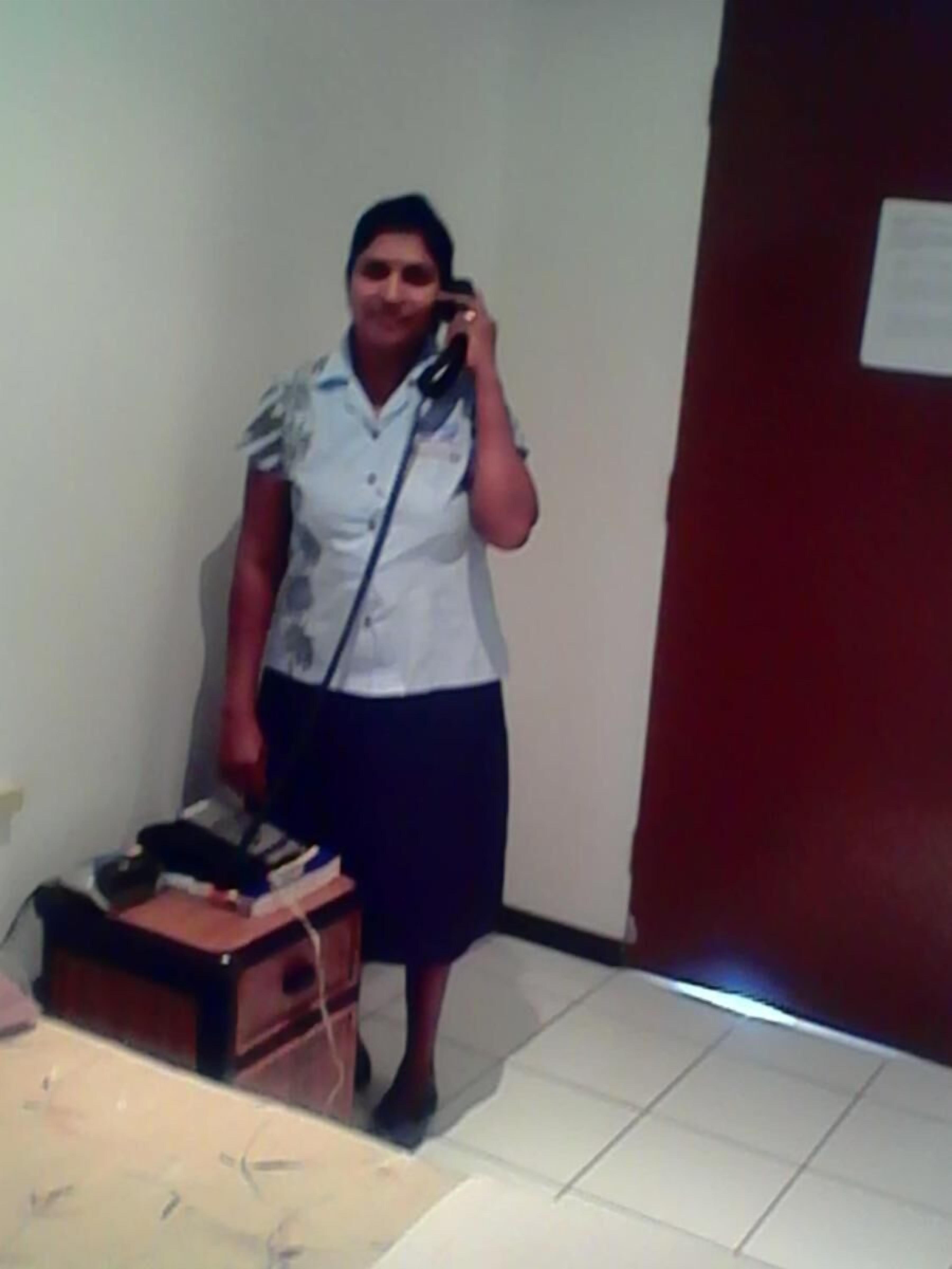 A person in a white shirt and dark skirt standing in a room with a desk and a chair.