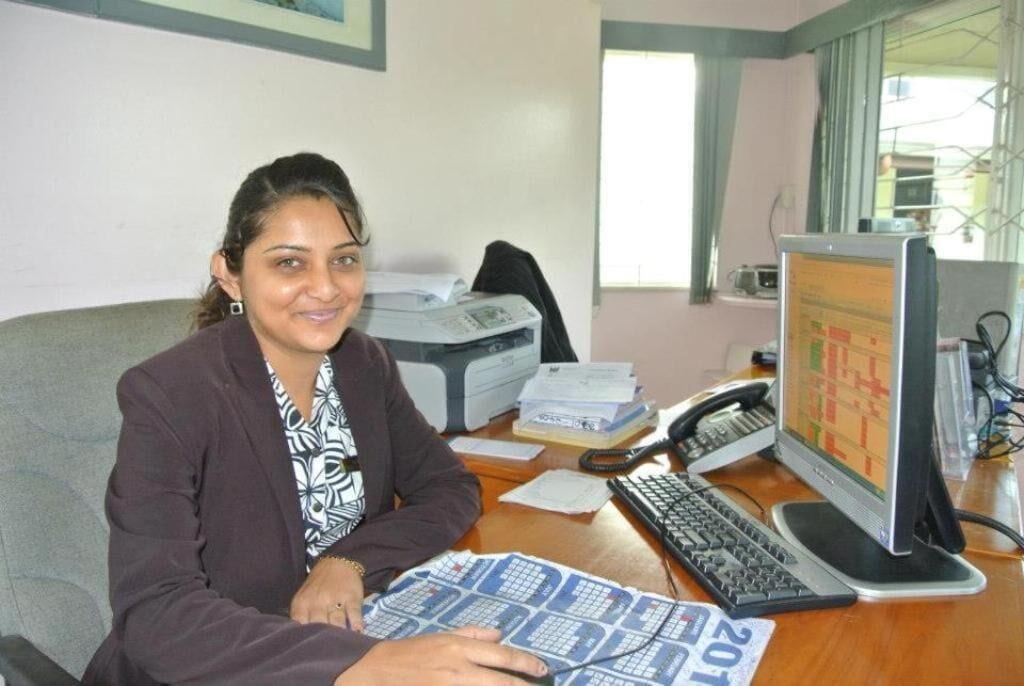 A person sitting at a desk with a computer, papers, and a telephone.