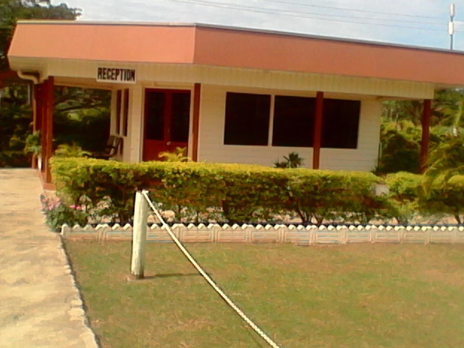 A reception area with a sign, a pathway, and a well-maintained hedge.
