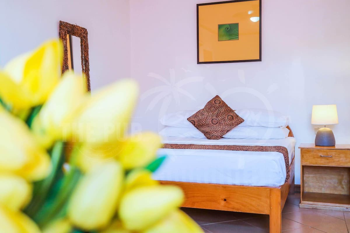 A neatly made bed with a patterned pillow, a bedside table with a lamp, and a framed picture on the wall.