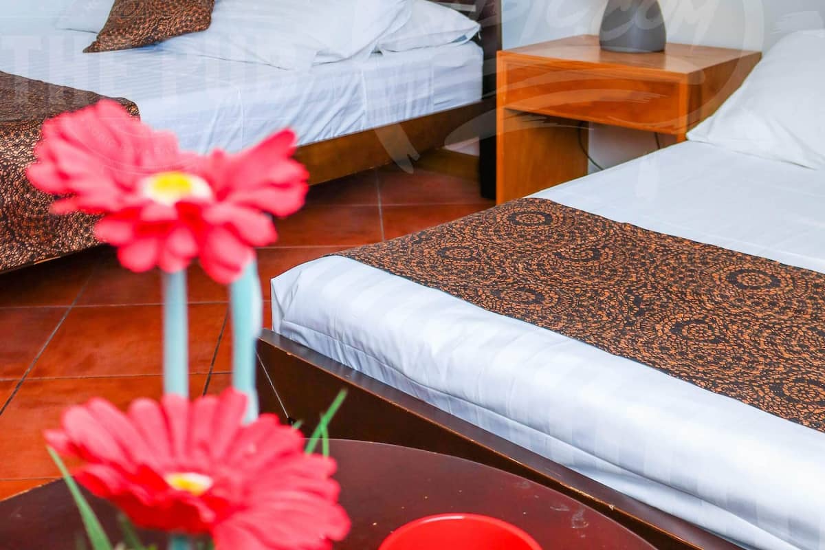 A hotel room with two beds, a nightstand with a lamp, and a table with a red cup and flowers.