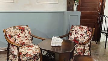 A pub hotel interior with two floral armchairs, a small wooden table, and a wooden door with "PUB HOTEL" sign.