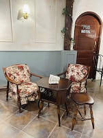 Interior de un hotel pub con dos sillones florales, una mesita de madera y una puerta de madera con el letrero 'PUB HOTEL'.