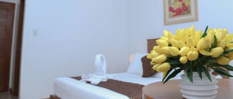 Una habitación de hotel con una cama, una silla blanca, una mesa blanca y un jarrón con flores amarillas.