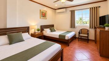 Habitación de hotel con dos camas, ventilador de techo, televisor, una silla y ventana con cortinas.