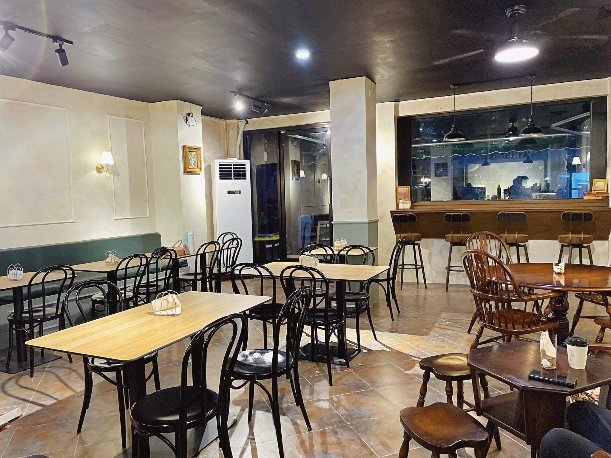 Un restaurante con mesas y sillas de madera, una zona de bar y vistas a la cocina a través de un muro de cristal.