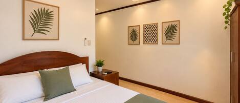 A hotel room with a bed, a ceiling fan, a nightstand with a plant, and wall art.