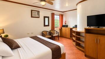 A hotel room with a bed, a desk, a television, and a ceiling fan.