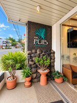 Entrada de un edificio con un letrero que dice 'The Pub' y una pared de piedra con plantas en macetas.