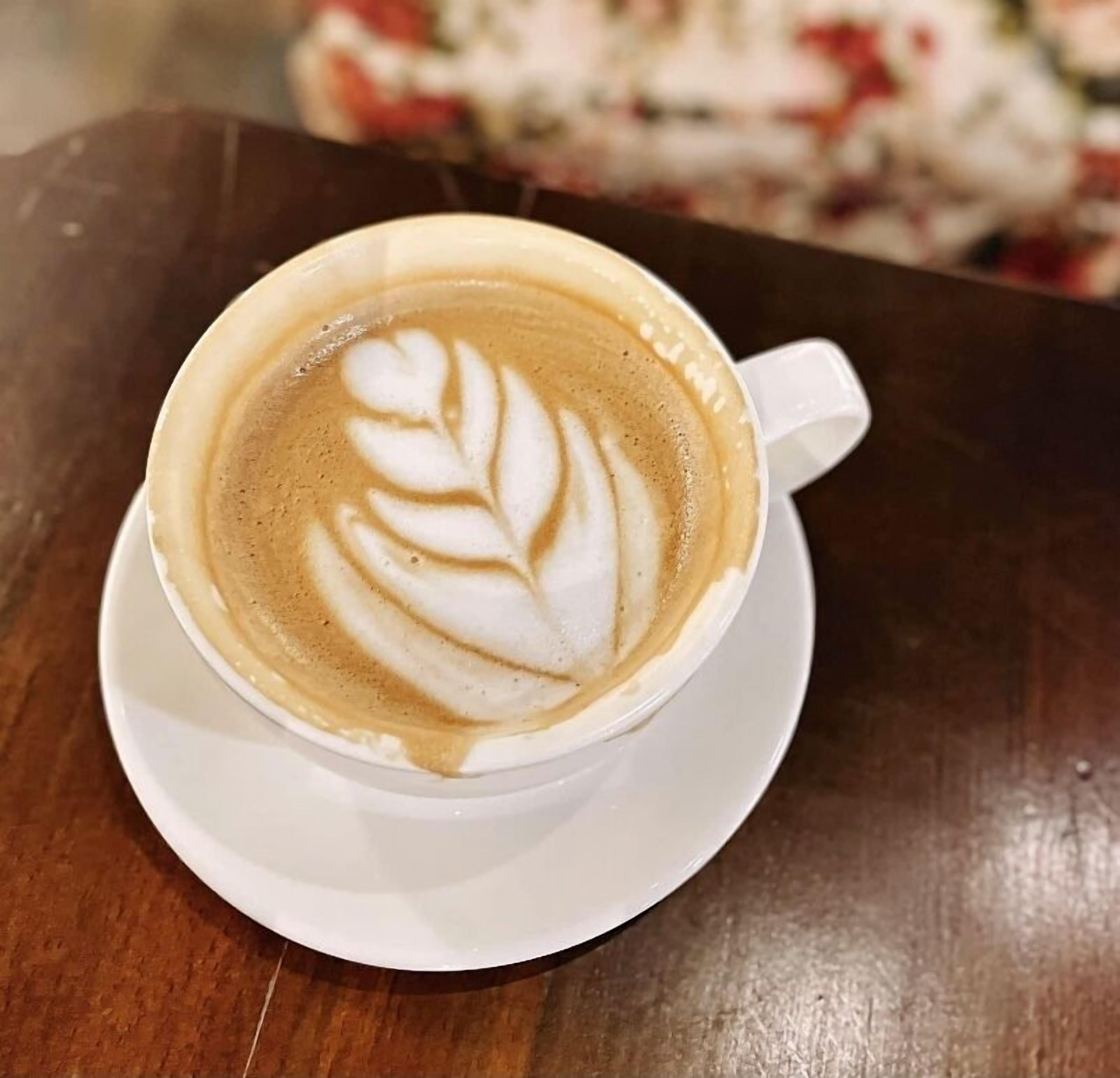 Une tasse de café surmontée d’un motif en latte art, posée sur une soucoupe blanche.