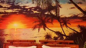 Una cama con un mural de atardecer, almohadas y una tarjeta de bienvenida.