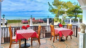 Un patio al aire libre con dos mesas dispuestas para comer, vista al mar y un árbol decorativo.