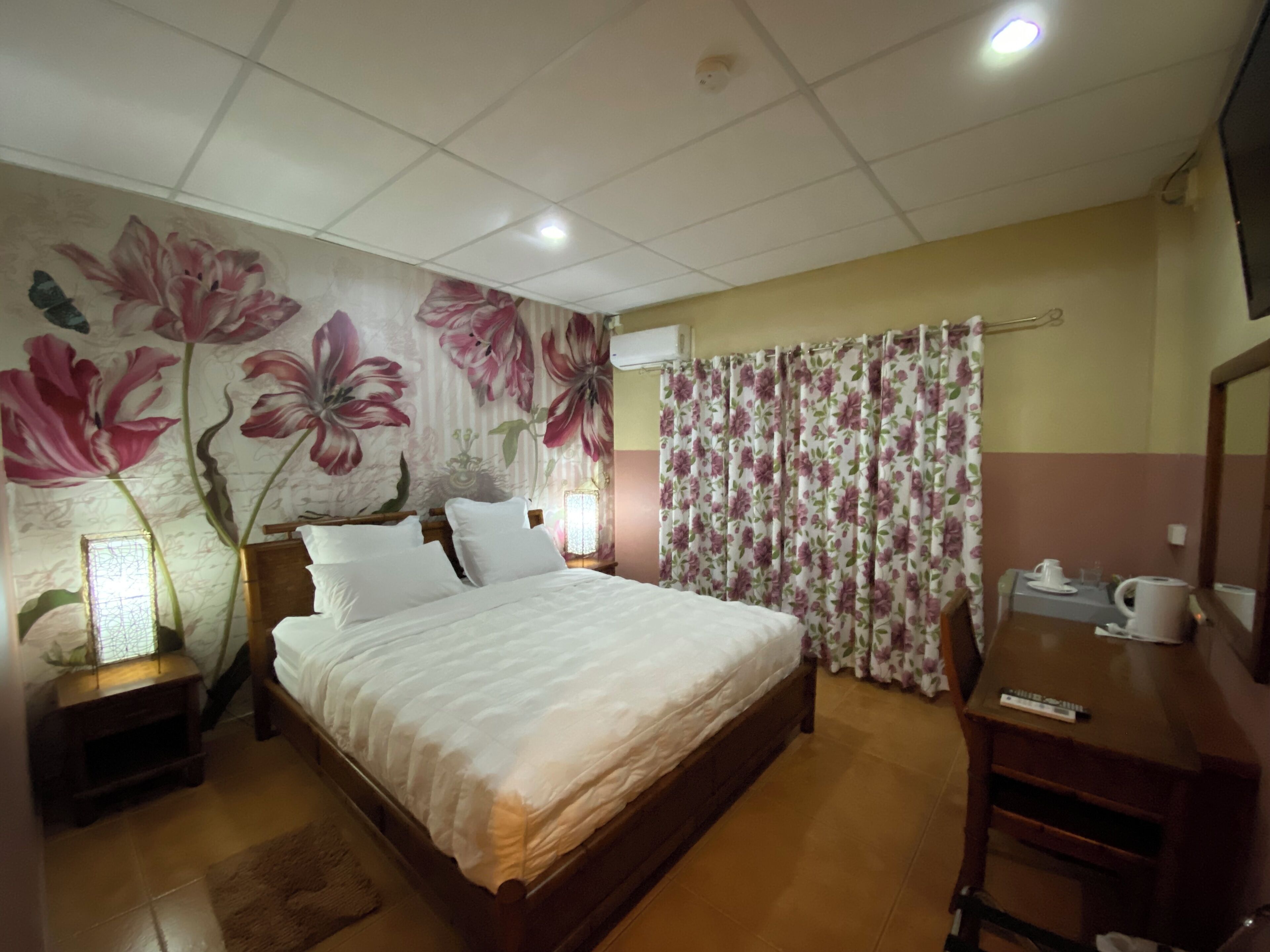A bedroom with a large bed, a nightstand, a dresser, a mirror, and a floral-patterned curtain.