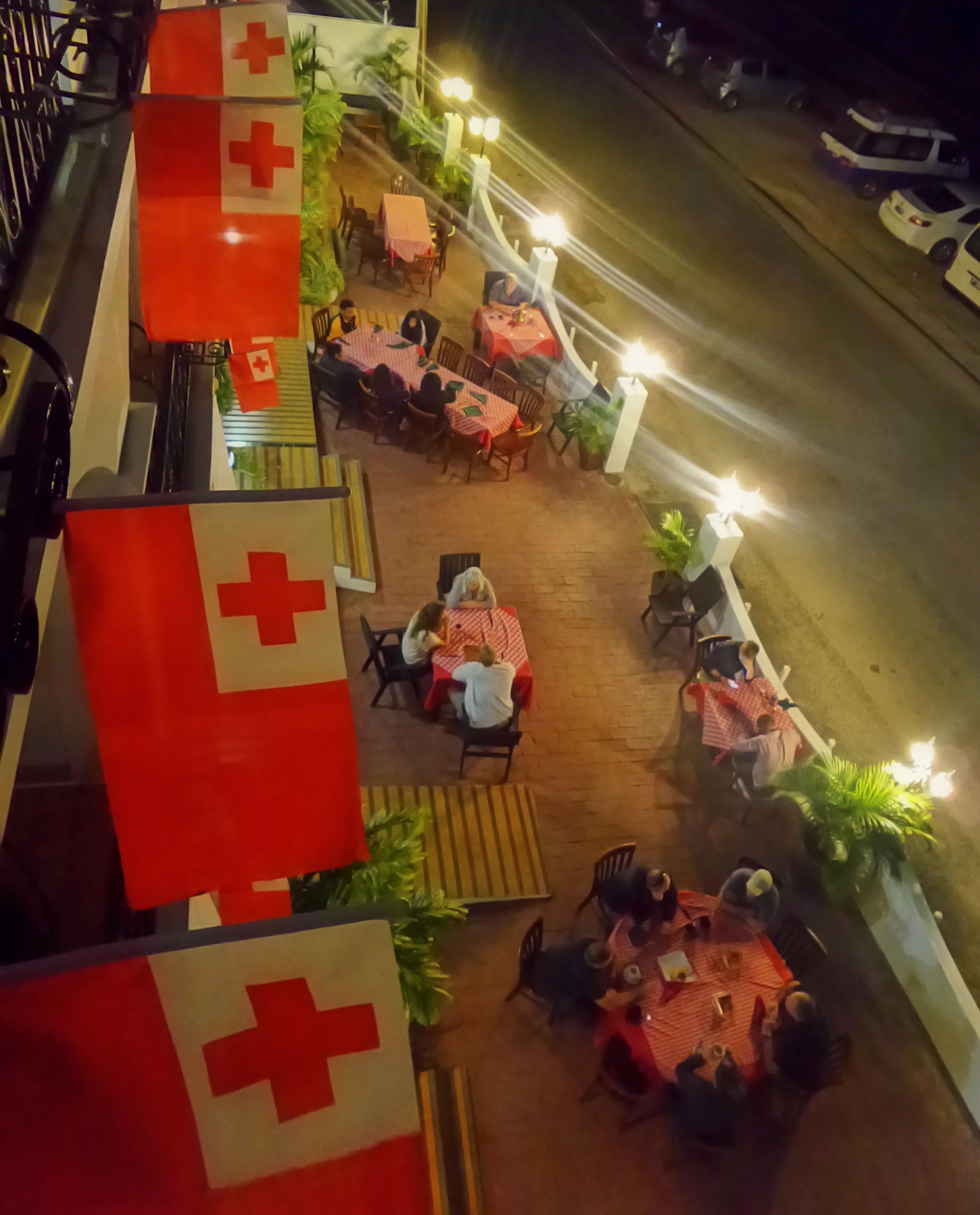 Un espacio exterior para comer con mesas y sillas, rodeado de plantas e iluminado por farolas.