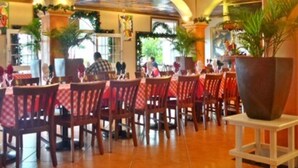 Un restaurante con piso de baldosas, manteles rojos a cuadros, sillas de madera y un techo decorativo.