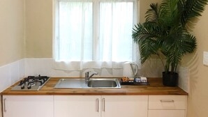 Une petite cuisine équipée d’une cuisinière à gaz, d’un évier et d’une fenêtre ornée de rideaux légers.