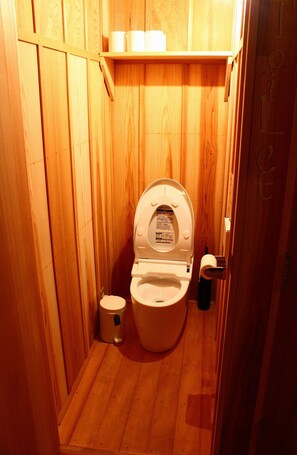 A wooden-paneled bathroom with a toilet, a small trash bin, and a shelf with toiletries. - Naramachi Hostel & Restaurant (Nara)