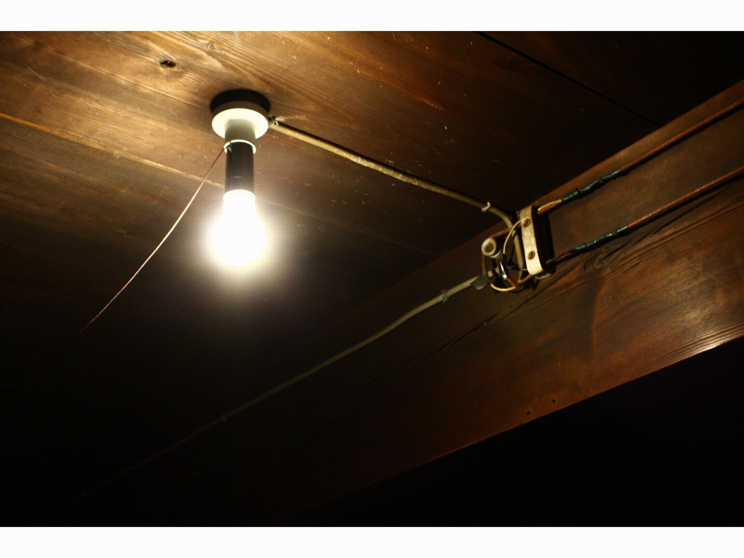 Un plafond avec des câbles apparents et une seule ampoule.