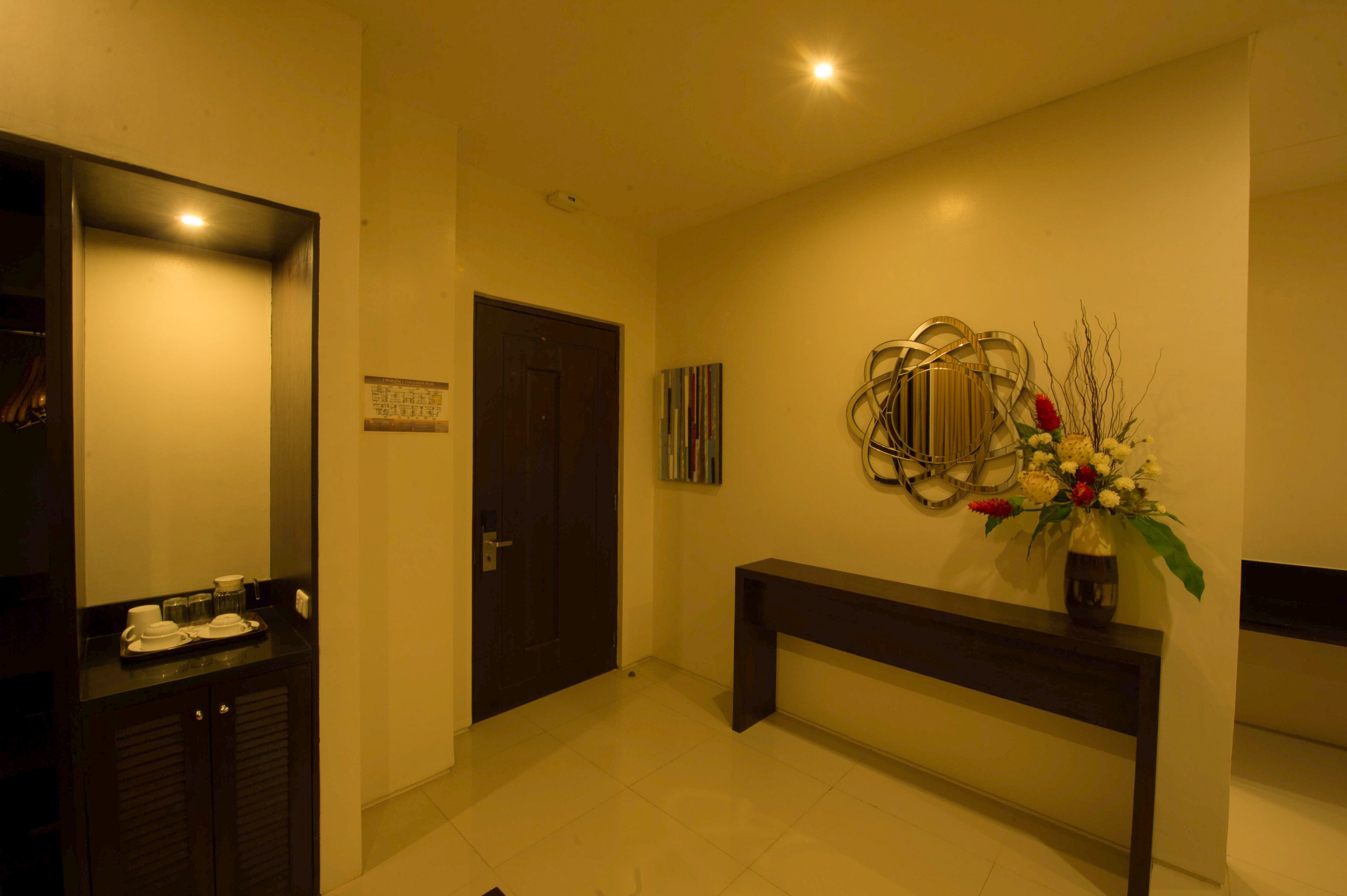 Un vestíbulo de hotel con mostrador de recepción, un banco de madera oscura, un espejo en la pared y un jarrón decorativo con flores.