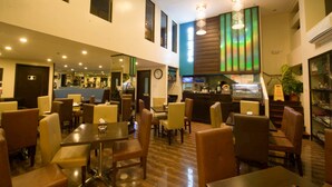 Een hotellobby met meerdere eetgedeeltes, een receptiebalie en een trap naar een hoger gelegen verdieping.