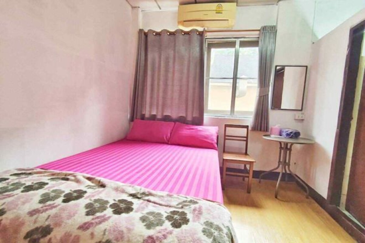 A small room with a bed, a chair, a small table, and a window with curtains.