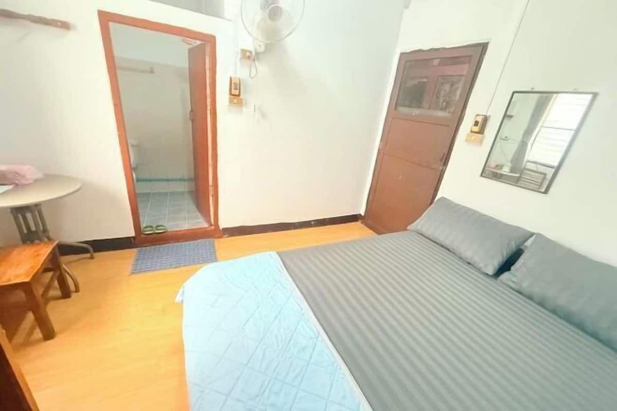 Une chambre à coucher avec un lit, un bureau, une chaise, une porte et un ventilateur.