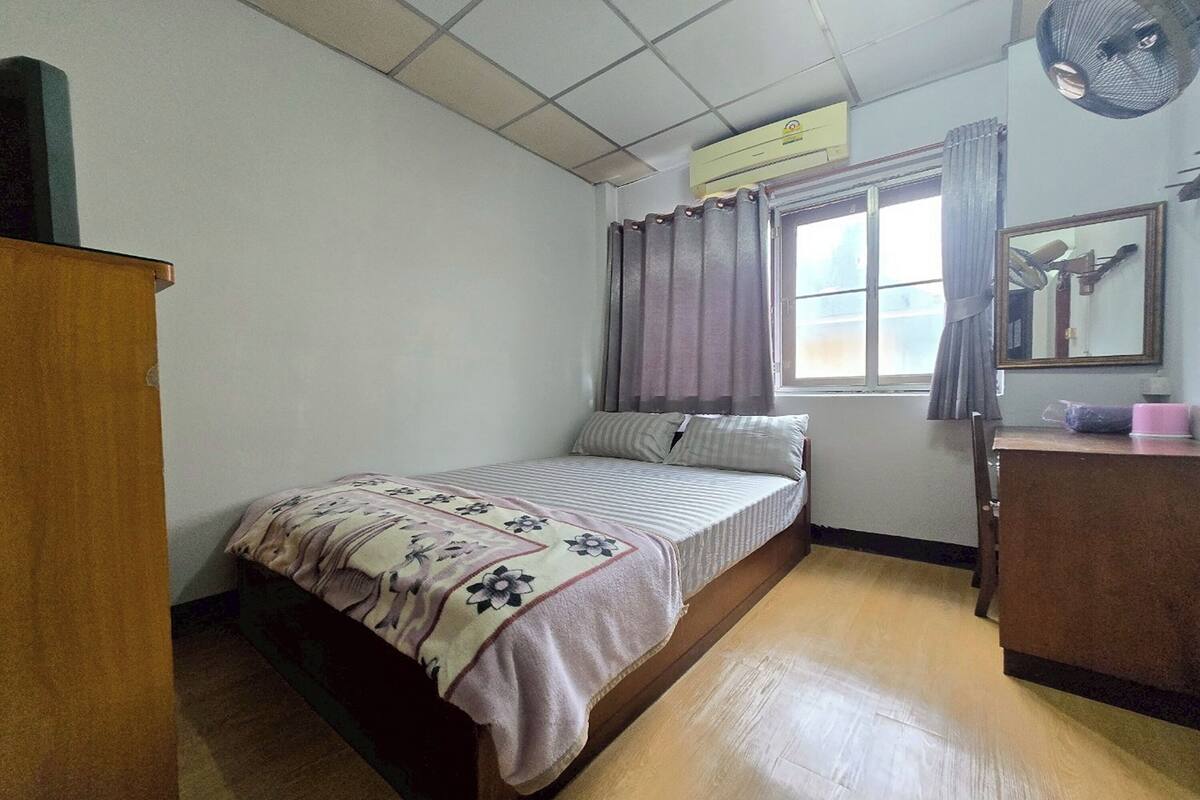 Une petite pièce simple, avec un lit, un bureau en bois, un miroir et une fenêtre avec des rideaux.