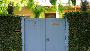 A blue gate with the number 7, surrounded by ivy-covered walls, leading to a building with a yellow facade. - Athelney Cottage (Hackney)