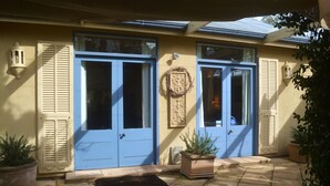A building with two blue doors, a small garden area with potted plants, and a tiled patio. - Athelney Cottage (Hackney)