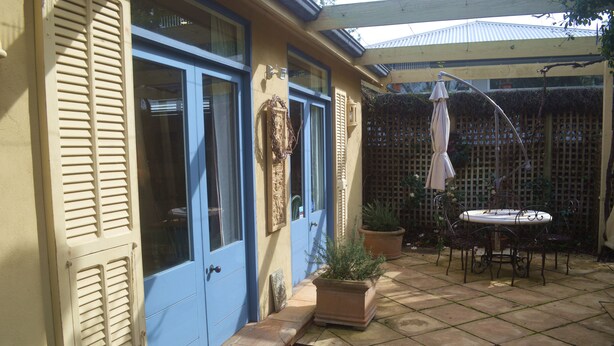 A patio with a table and chairs, a potted plant, and a door with shutters. - Athelney Cottage (Hackney)