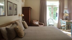 A bedroom with a large bed, two chairs, a desk, and a window with curtains. - Athelney Cottage (Hackney)