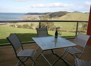 A balcony with a glass table and metal chairs, overlooking a coastal landscape with hills and a body of water. - Black Rock Retreat (Howth)
