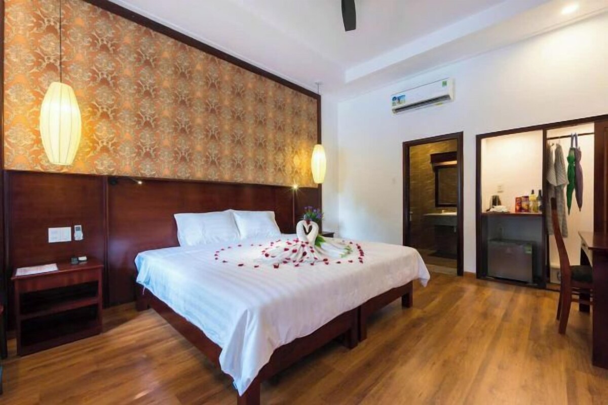 A hotel room with a wooden bed, a nightstand, a desk, and a wardrobe.