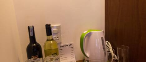 A table with a mini bar setup including wine bottles, glasses, a teapot, and a kettle.
