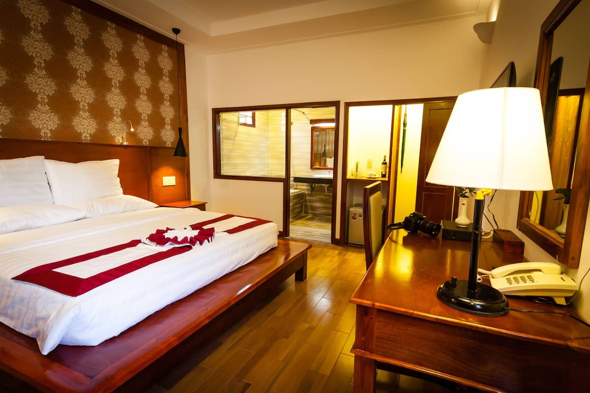 A hotel room with a bed, a desk with a lamp, a telephone, and a mirror.