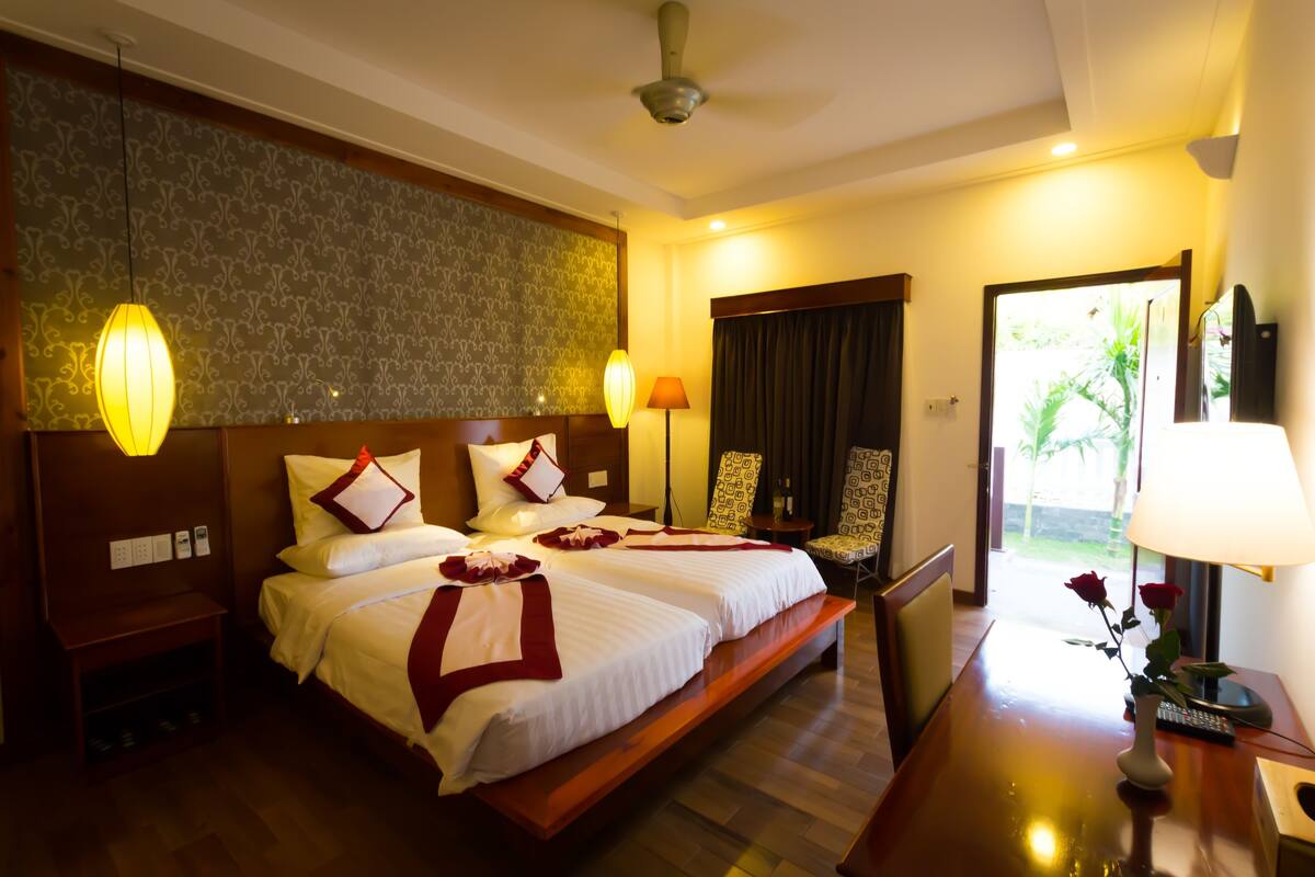 A hotel room with a large bed, two bedside tables, a desk with a lamp, a chair, and a view of the outdoors.