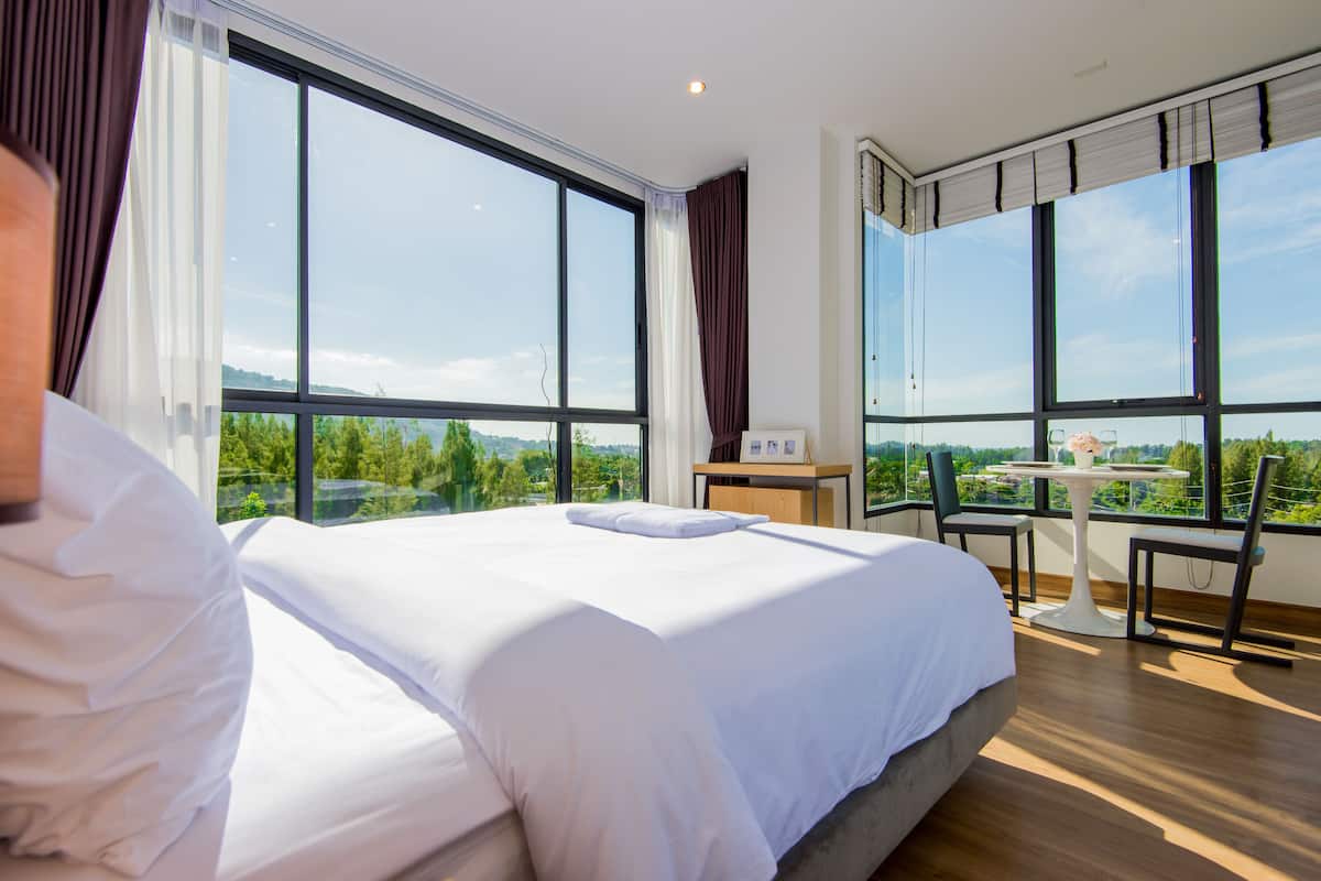 Quarto de hotel moderno com uma cama grande, uma mesinha com cadeiras e amplas janelas com vista para o exterior.