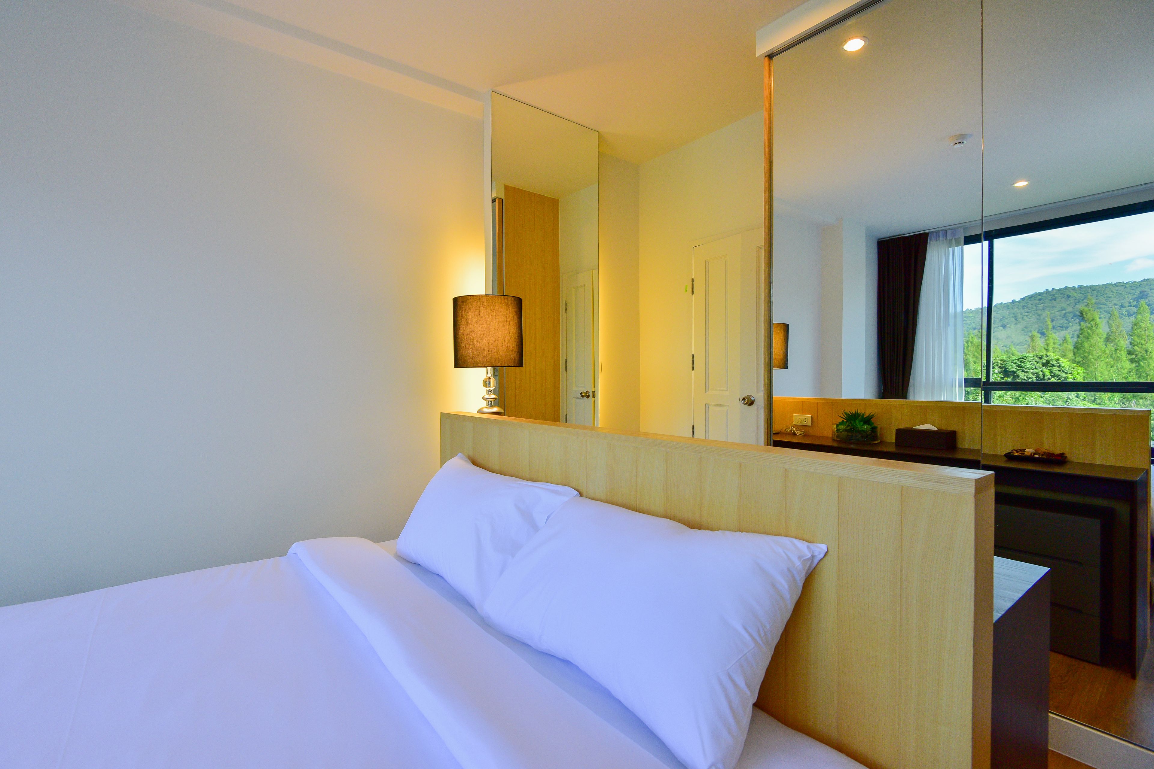 Habitación de hotel moderna con una cama grande, una lámpara de noche, un espejo y vistas al exterior.